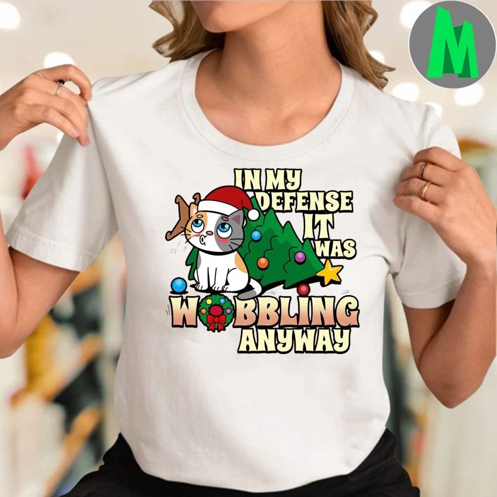 It Was Wobbling Anyway A cat wearing a Santa hat sits next to a fallen Christmas tree T-Shirt